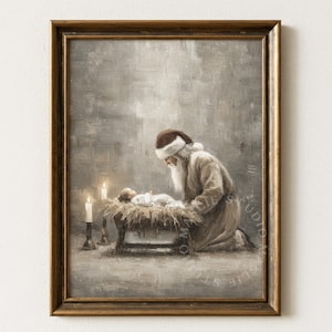 May include: A framed painting shows a kneeling Santa Claus figure looking at a baby in a manger. The artwork uses soft, muted tones, with lit candles and a warm atmosphere. The painting is set in a gold-coloured frame.