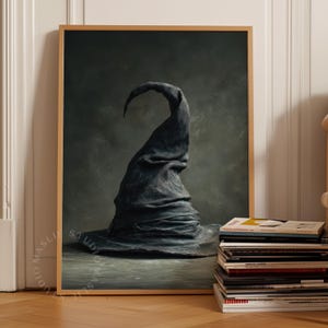 May include: A framed wall art print featuring a dark, weathered, pointed hat with deep folds and a curved tip. The hat is rendered in shades of charcoal and slate grey against a moody, textured background. The frame is a light-toned wood finish.