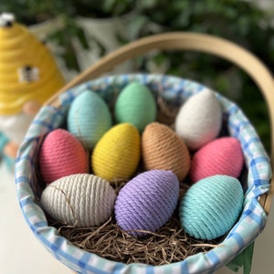Puede incluir: Una cesta a cuadros azules y blancos llena de huevos de Pascua de lana de colores. Los huevos están hechos de lana y son de varios colores, incluyendo rosa, morado, amarillo, verde y azul.