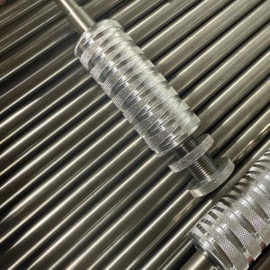 May include: A silver-colored metal knurling tool featuring a cylindrical body with a cross-hatched textured grip, a smooth shaft at one end, and a threaded adjustment knob at the other, resting atop a collection of parallel metal rods.