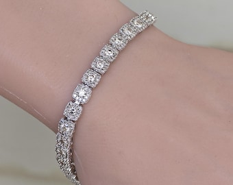 May include: A sparkling silver bracelet with square-cut, clear gemstones. The bracelet is worn on a wrist and catches the light, showcasing its brilliant facets. The design is elegant and suitable for special occasions.