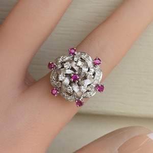 May include: A silver ring with a large, white diamond center surrounded by smaller diamonds and pink rubies.