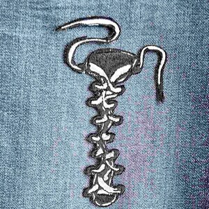 May include: A black and white embroidered patch of a scorpion with a segmented tail and a curled stinger. The scorpion is on a blue denim background.