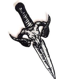 May include: Black and white embroidered patch in the shape of a dagger. The dagger features a detailed handle, a blade, and a decorative design with horns. The patch is set against a white background.