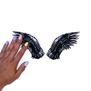 May include: A pair of black embroidered angel wings, with a detailed design, on a white background.