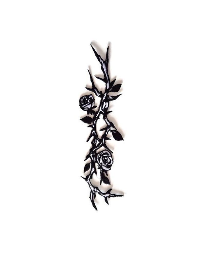 K&ouml;nnte beinhalten: Ein schwarz-wei&szlig;es Blumendesign mit Rosen, Dornen und Bl&auml;ttern. Das Design ist vertikal ausgerichtet und scheint ein Aufn&auml;her oder eine Applikation zu sein, mit einer detaillierten, k&uuml;nstlerischen &Auml;sthetik. Das Bild ist vor einem wei&szlig;en Hintergrund.
