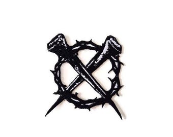 Puede incluir: Parche negro con dos clavos cruzados dentro de una corona de espinas. El diseño es una imagen de alto contraste, con los clavos y la corona en negro sólido sobre un fondo blanco. El parche es probablemente para ropa o accesorios.