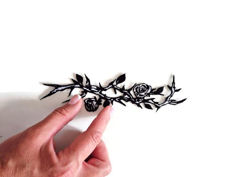 K&ouml;nnte beinhalten: Schwarzer floraler Zweig mit Rosen und Dornen. Das Design zeigt zwei Rosen und mehrere Bl&auml;tter. Das Bild befindet sich auf wei&szlig;em Hintergrund.