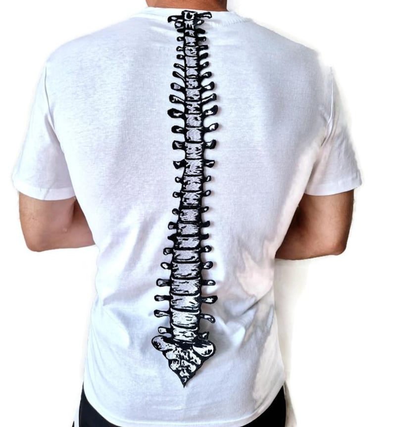 Puede incluir: Camiseta blanca con un dise&ntilde;o de columna vertebral en blanco y negro impreso en la espalda. La ilustraci&oacute;n de la columna vertebral es vertical. La camiseta tiene mangas cortas y cuello redondo.