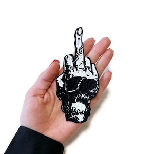 May include: Black and white embroidered iron-on patch of a skull giving the middle finger.