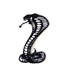 May include: A black and white embroidered cobra patch. The snake is shown with its hood flared, tongue extended, and scales detailed with white thread. The patch is set against a white background.