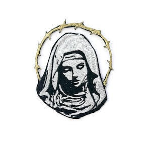 May include: A black and white embroidered patch of a woman wearing a white hood with a gold thorn crown around her head.
