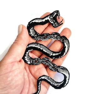 May include: Black and white embroidered iron-on patch of a snake with chains wrapped around its body. The snake's mouth is open and its fangs are visible.