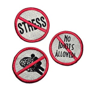 May include: Three embroidered patches with red borders and crossed-out designs. One says "STRESS", another "NO IDIOTS ALLOWED!", and the third depicts a person carrying a brain. The patches are on a light gray background.