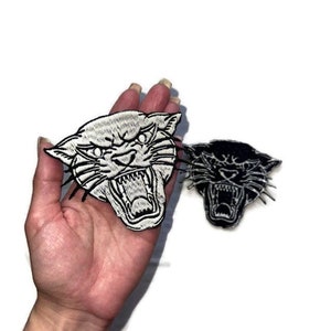 May include: Two embroidered iron-on patches of a snarling panther head. One patch is black and white, the other is black.