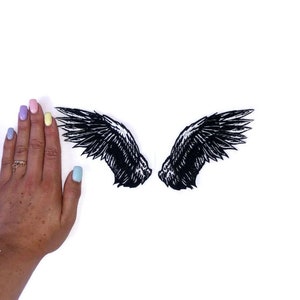 May include: Two black embroidered angel wings on a white background. The wings are about the size of a hand.