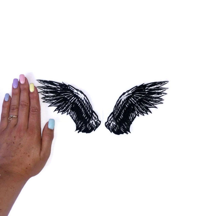 May include: Two black embroidered angel wings on a white background. The wings are about the size of a hand.
