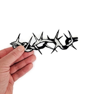 Pode incluir: Etiqueta bordada preta de ferro de uma coroa de espinhos espinhosa.