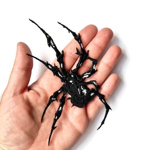 May include: Black embroidered spider patch with white details. The patch is about the size of a hand.