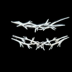 Op de afbeelding: Twee zilverkleurige, gestileerde doornenkronen, een boven de andere, op een zwarte achtergrond.