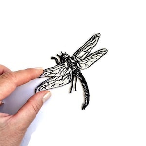 Könnte beinhalten: Schwarzer und weißer gestickter Libellen-Patch. Die Libelle ist im Flug mit ausgebreiteten Flügeln.