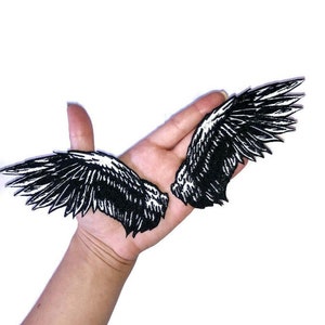 May include: Two black embroidered iron-on patches of angel wings. The wings are detailed with white stitching.