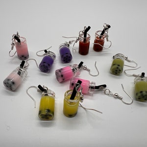 May include: A collection of 10 pairs of bubble tea earrings. The earrings are made of clear plastic and feature a variety of colors, including pink, purple, green, yellow, and red. Each earring has a black straw and silver hook.