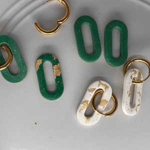 May include: A set of green and white oval-shaped earrings with gold accents. The earrings are made of a textured material and have a simple, modern design.