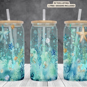 May include: Three clear glass tumblers with lids and straws, featuring a watercolor design of seashells, starfish, and seaweed in shades of blue, green, and gold.  The tumblers are on a white wood surface.  "IN THIS LISTING 1 FREE DESIGNS INCLUDED" is printed on a white label.