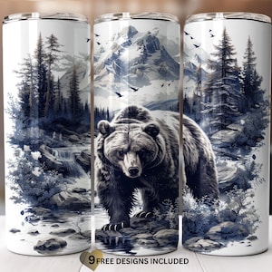 May include: A stainless steel tumbler with a graphic of a brown bear standing in a forest with a waterfall and mountains in the background. The tumbler is white with blue and gray accents.
