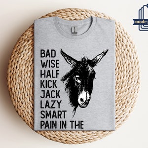 May include: Gray t-shirt with a black and white illustration of a donkey's head. The text "Bad Wise Half Kick Jack Lazy Smart Pain in the" is printed on the shirt.