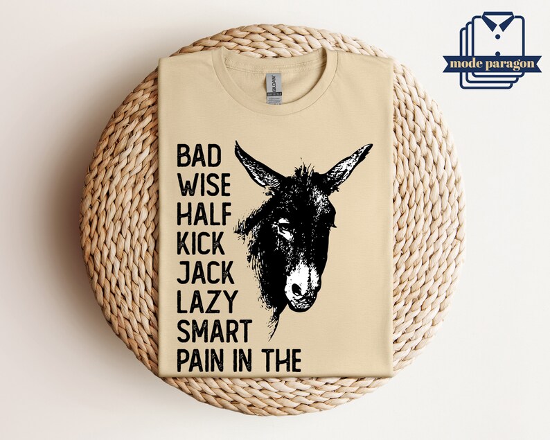 May include: A tan t-shirt with a black and white illustration of a donkey's head. The text "Bad Wise Half Kick Jack Lazy Smart Pain in the" is printed on the shirt.