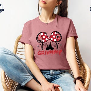 May include: A pink t-shirt with a red and white Minnie Mouse ears design and the word "GRAMMY" printed on the front. The ears have white polka dots and a red bow. The design also includes a silhouette of Cinderella's castle.