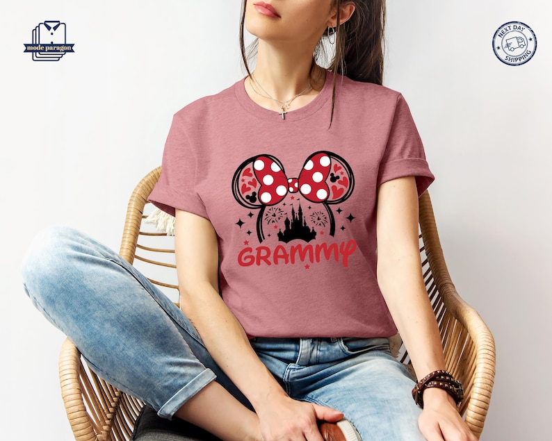 May include: A pink t-shirt with a red and white Minnie Mouse ears design and the word "GRAMMY" printed on the front. The ears have white polka dots and a red bow. The design also includes a silhouette of Cinderella's castle.