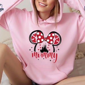 Puede incluir: Sudadera con capucha rosa claro con un dise&ntilde;o de Minnie Mouse. El dise&ntilde;o incluye un lazo rojo y blanco con lunares, orejas en forma de coraz&oacute;n, un castillo negro y la palabra "mam&aacute;" en escritura roja.