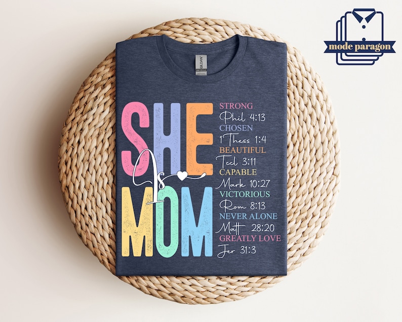 May include: A navy blue t-shirt with a rainbow colored graphic that says "She is Mom" with bible verses listed below. The verses are: Phil 4:13, 1 Thess 1:4, Tel 3:11, Mark 10:27, Rom 8:13, Matt 28:20, Jer 31:3.