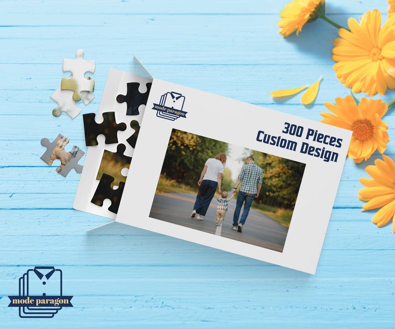 May include: A white puzzle box with the text "300 Pieces Custom Design" and a family photo. Several puzzle pieces are scattered around the box. Yellow flowers are in the background. The box has the "mode paragon" logo.