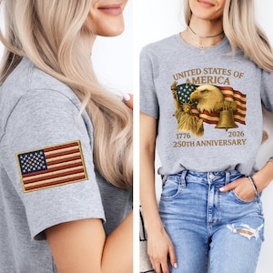 Puede incluir: Una camiseta gris con un parche bordado de la bandera estadounidense en la manga. La otra camiseta tiene un gr&aacute;fico de un &aacute;guila, una bandera y la Campana de la Libertad con el texto "UNITED STATES OF AMERICA 1776 2026 250TH ANNIVERSARY".
