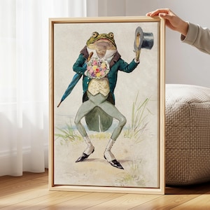 May include: A framed art print featuring a dapper frog in a teal coat, holding a bouquet and a top hat. The frog is wearing a vest, light green pants, and black shoes. The background shows a beach scene with grass and water.