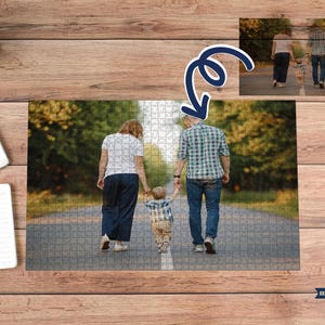 May include: A family walking on a paved path, captured in a jigsaw puzzle. The puzzle shows a couple and a child holding hands, with a blurred background of trees. The puzzle is on a wooden surface, with a small plant, a phone, and a notepad.