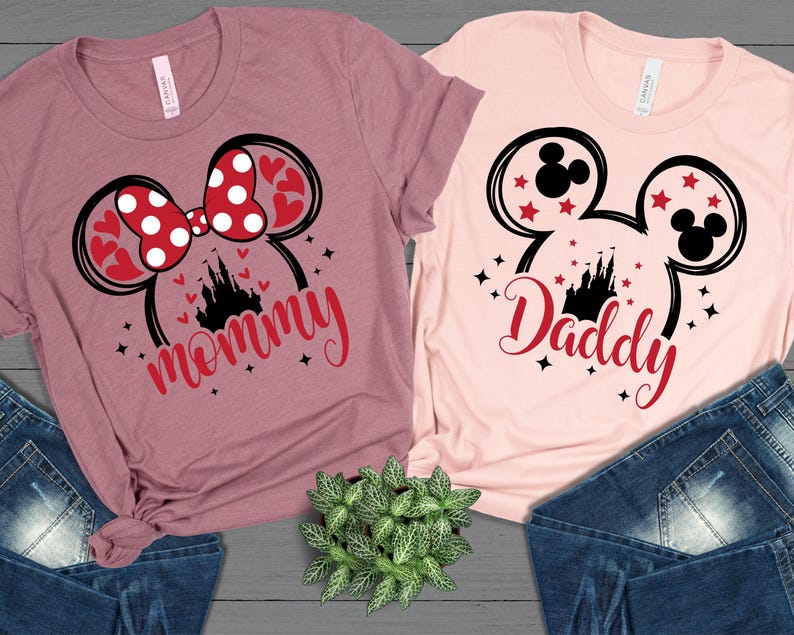 Puede incluir: Dos camisetas con dise&ntilde;os tem&aacute;ticos de Disney. Una es malva con un lazo de Minnie Mouse y la palabra "mam&aacute;" en escritura roja. La otra es rosa claro con orejas de Mickey Mouse y la palabra "pap&aacute;" en escritura roja. Ambas camisetas tienen un castillo.