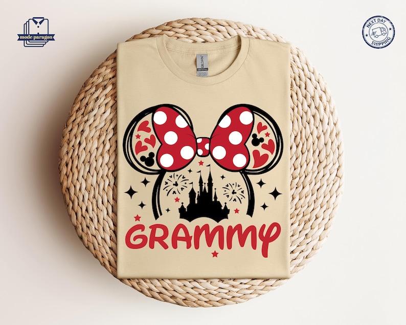 May include: A tan t-shirt with a black silhouette of Cinderella's castle and a red and white Minnie Mouse bow. The text "GRAMMY" is printed in red below the image.
