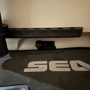 May include: A close-up of a black plastic component with the word "SEA" in large, silver letters. Above it is a black, rectangular piece with several rectangular cutouts. A small, black lever is visible.