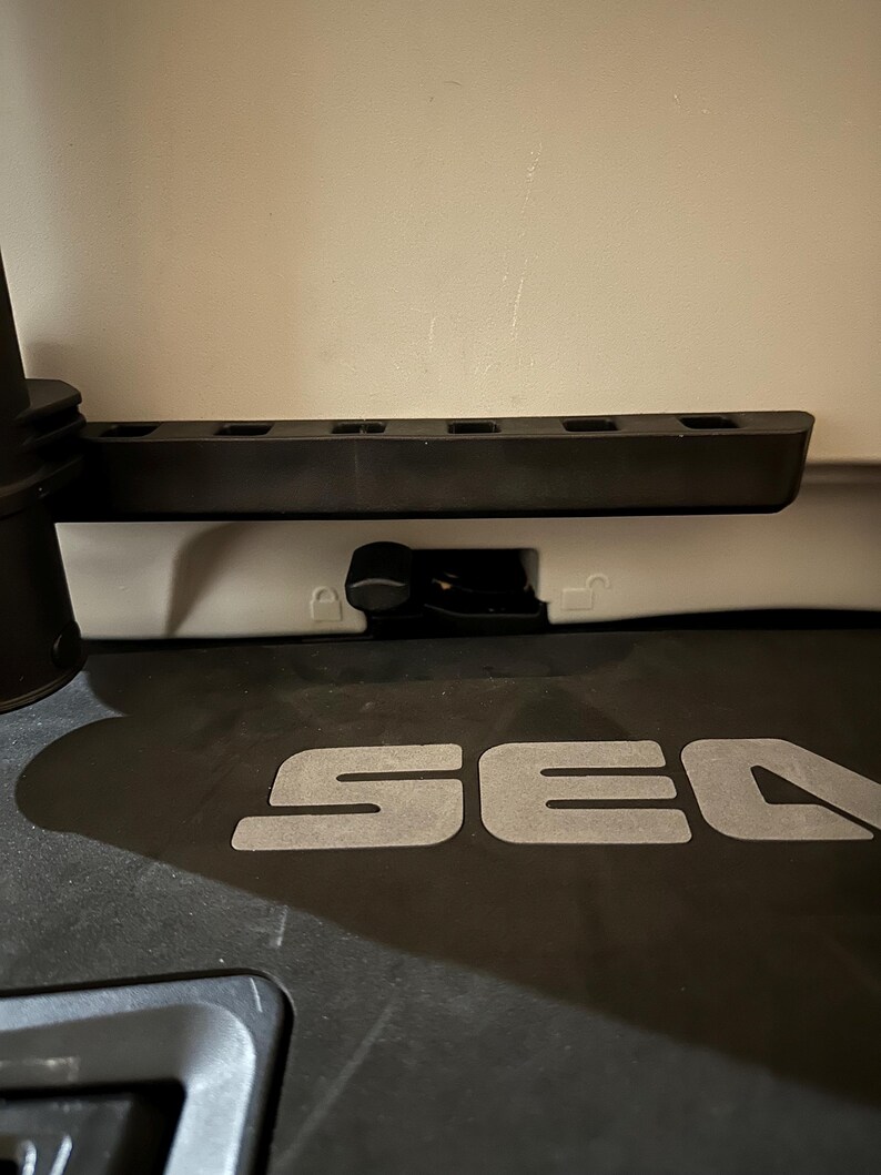 May include: A close-up of a black plastic component with the word "SEA" in large, silver letters. Above it is a black, rectangular piece with several rectangular cutouts. A small, black lever is visible.