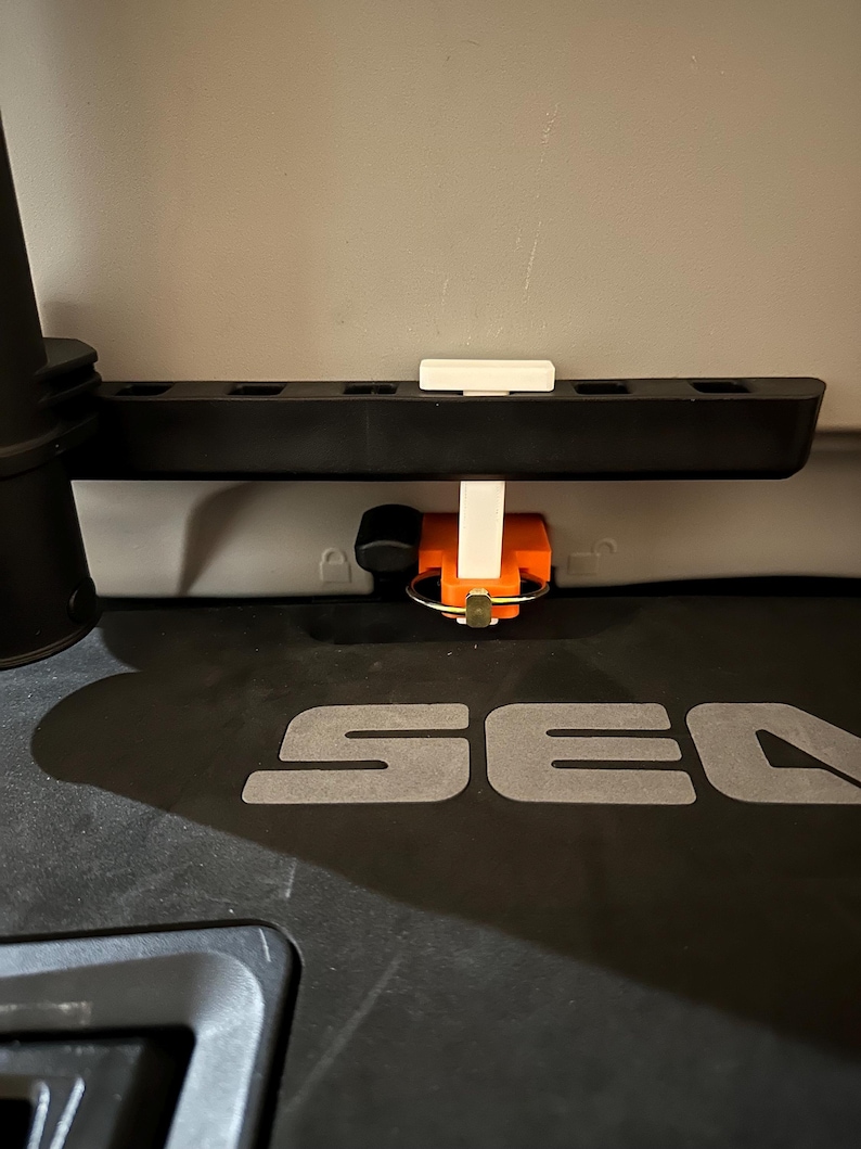 May include: A black plastic rack with multiple slots, a white support, and an orange and black component with a metal ring. The word "SEA" is visible in grey on a black surface.