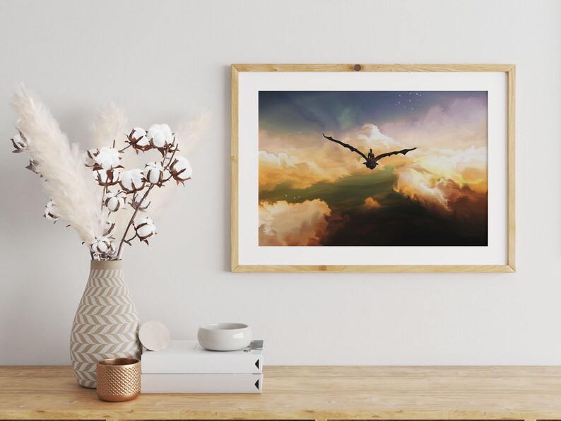 Op de afbeelding: Een ingelijste print van een silhouet van een persoon die op een draak rijdt die door een bewolkte lucht vliegt met een zonsondergang op de achtergrond.