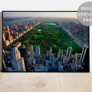 以下が含まれることがあります： ニューヨーク市のセントラルパークの航空写真。マンハッタンの超高層ビルが前景と背景に写っています。公園は鮮やかな緑色で、木々や道が確認できます。街の建物は、近代的なものと伝統的なものが混在しています。