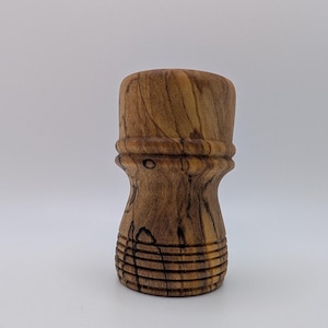 May include: A handcrafted wooden shaving brush handle. The handle is made of a light brown wood with dark brown grain patterns. The design features a bulbous top, a decorative midsection, and a grooved base.