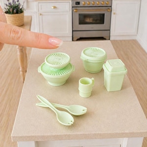 Peut inclure: Ensemble de miniatures de cuisine vert clair, comprenant des bols, une tasse, une poubelle et des cuillères de service. Les articles sont disposés sur un comptoir de couleur claire, suggérant une maison de poupée ou une cuisine miniature.