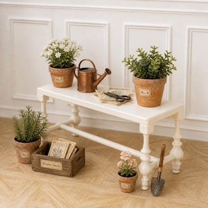 May include: A miniature gardening scene featuring a white bench with terracotta pots holding plants. A small copper watering can, a wooden box labeled "Flower Seeds", and a trowel complete the setup. The pots are labeled with numbers.
